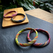 Load image into Gallery viewer, Colorful woven bracelets on a dark surface with a wooden coaster in the background.