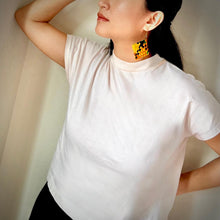 Load image into Gallery viewer, Person wearing a white t-shirt and colorful earrings against a neutral background
