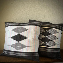 Load image into Gallery viewer, Two patterned pillows on a wooden surface with a neutral wall background
