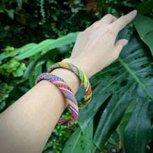 Load image into Gallery viewer, Colorful braided bracelet on a wrist with a green leafy background
