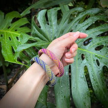 Load image into Gallery viewer, Hand wearing colorful bracelets with a tropical leaf background

