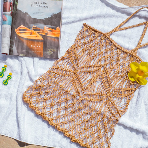 abaca fiber macrame tote bag on beach towel beside magazine, yellow flower and green earrings