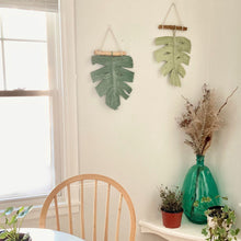 Load image into Gallery viewer, Light green and dark green monstera leaf hanging wall decor inside home with aqua vase and three indoor plants
